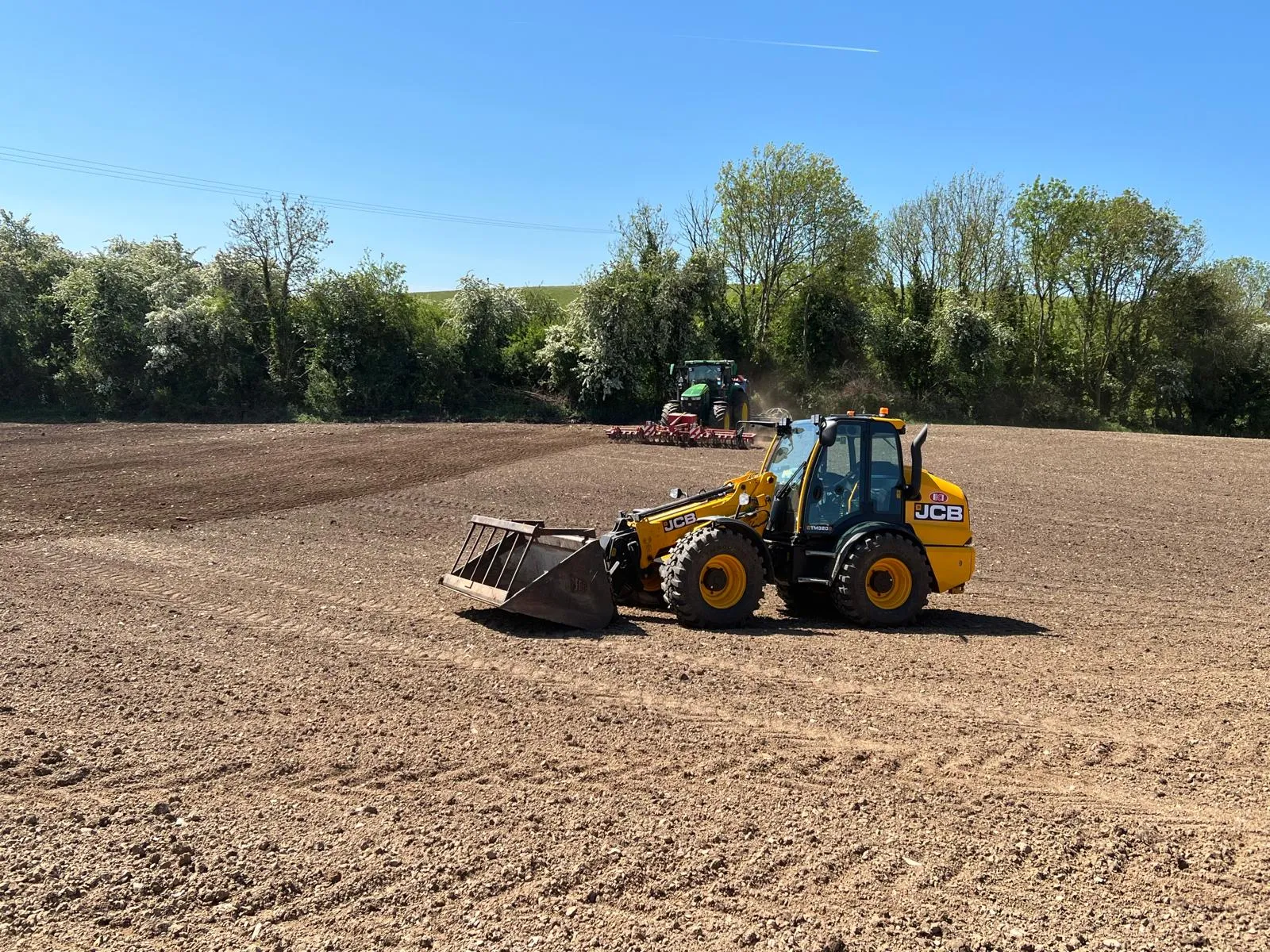 JCB loader and tractor working in open field preparing seedbed